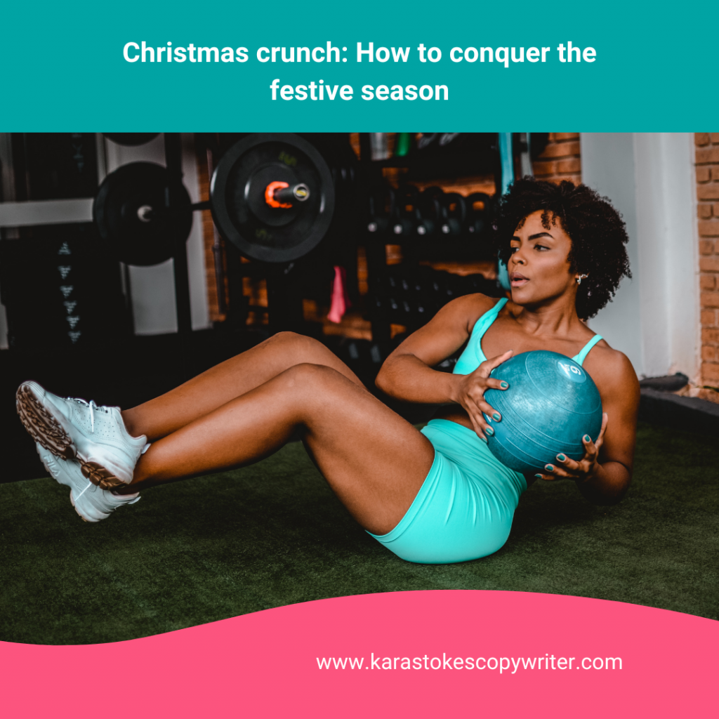 A woman wearing aqua shorts and sports bra is doing a crunch while holding a medicine ball.