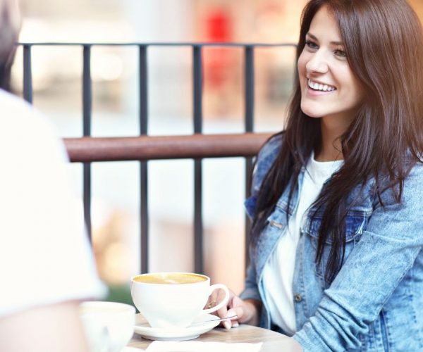 Brunette woman sitting at a cafe table smiling at a man.