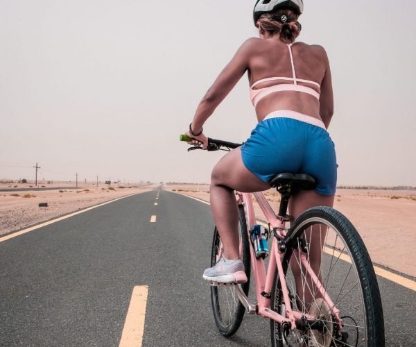 Woman-bike-ride-road Woman in a sports brad and blue bike shorts sitting on a bike on a road.