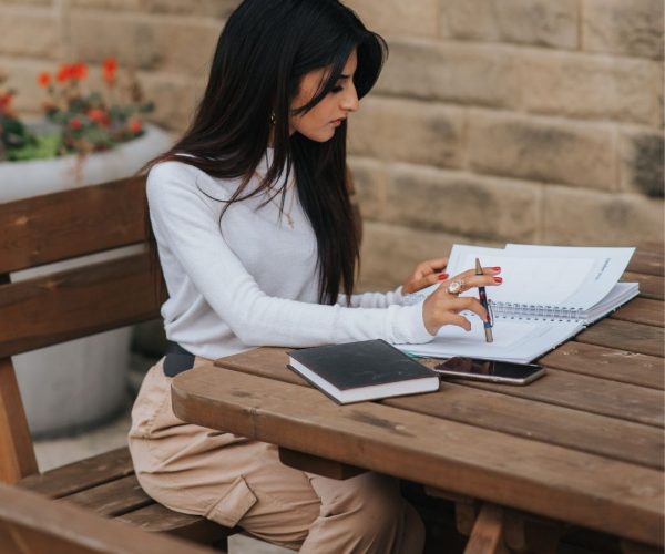 Woman-notebook-pen-thinking Woman creating content in a notebook at a wooden table.