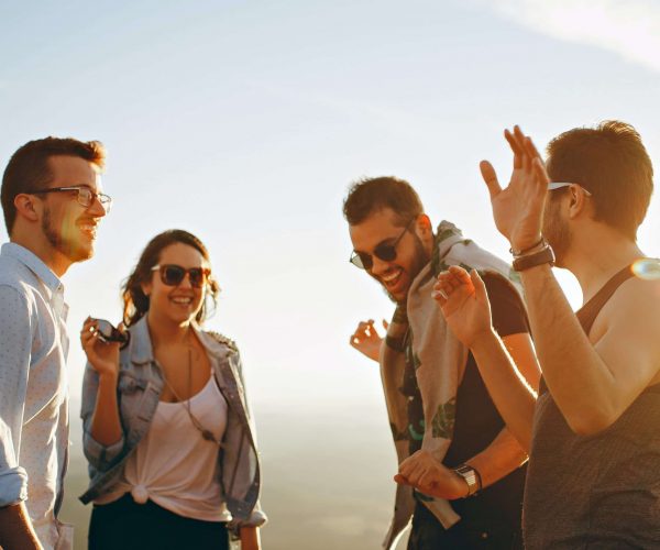 pexels-helena-lopes-708392 Three men and one woman are laughing and talking at the top of hill at sunset.